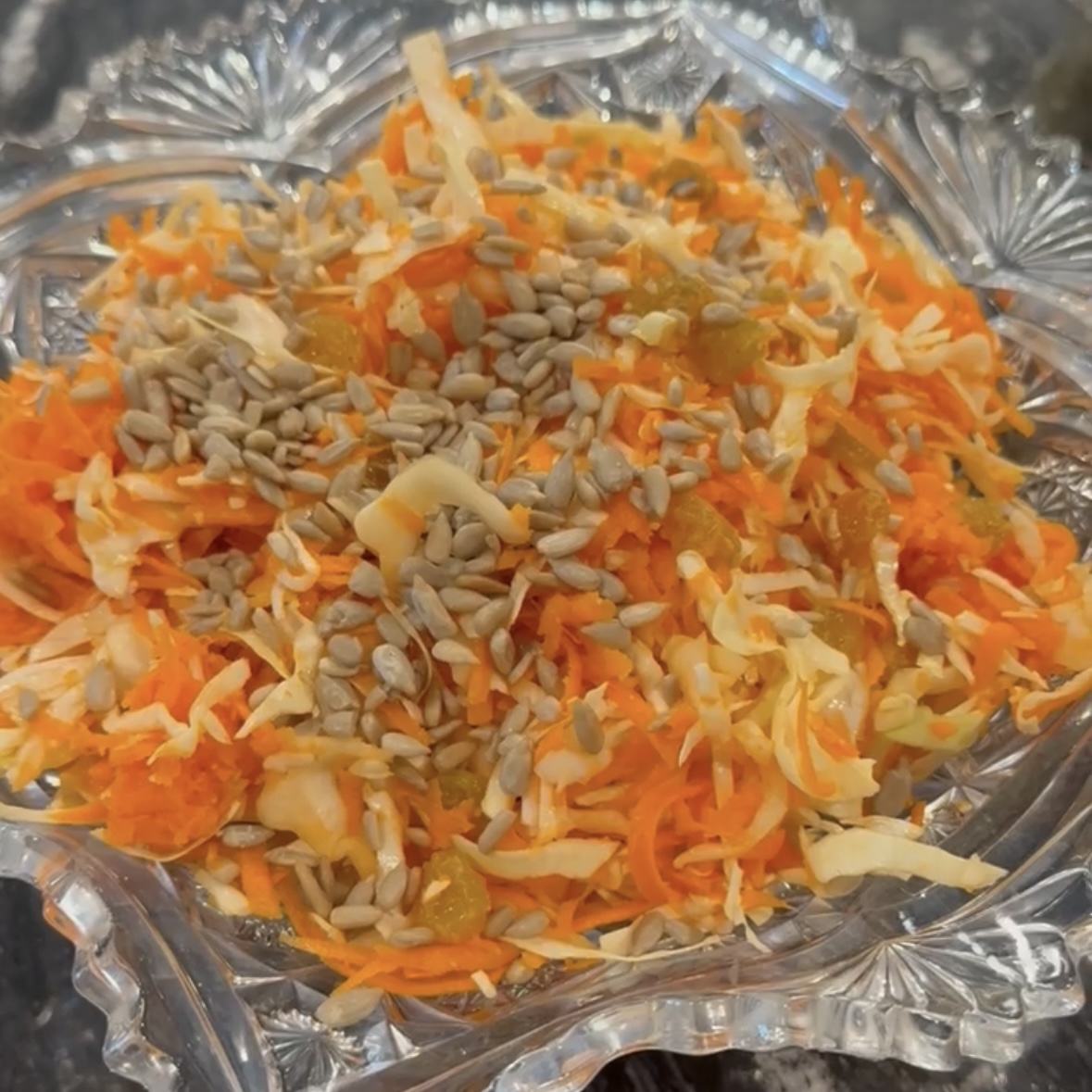 Crystal bowl of cabbage carrot slaw garnished with golden raising and sunflower seeds