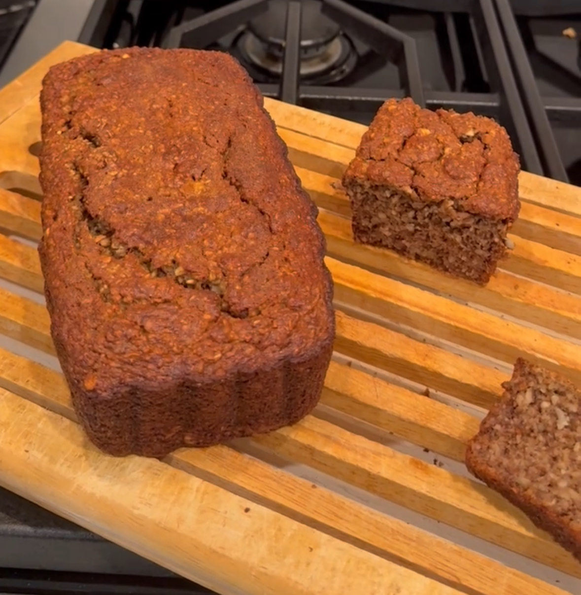 A loaf of banana oatmeal nut bread sitting on a bamboo cooling rack.